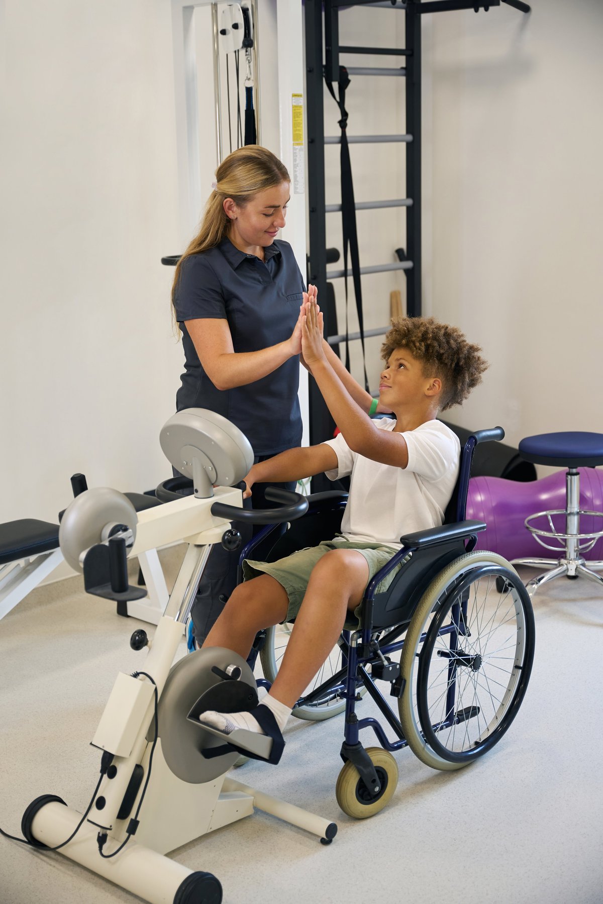 Therapist supervises a young patient during an arm bike exercise